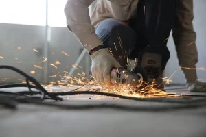 Worker using an angle grinder on the floor, creating sparks during metal cutting on a construction site.